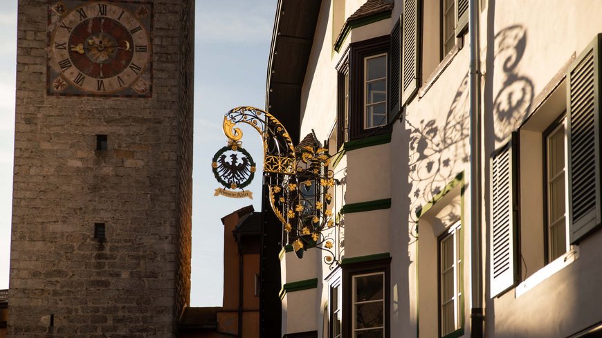 Exzellent essen in diesem Restaurant in Sterzing Historische Uhr an Steinturm neben Gebäude mit dekorativem Schild und Schatten