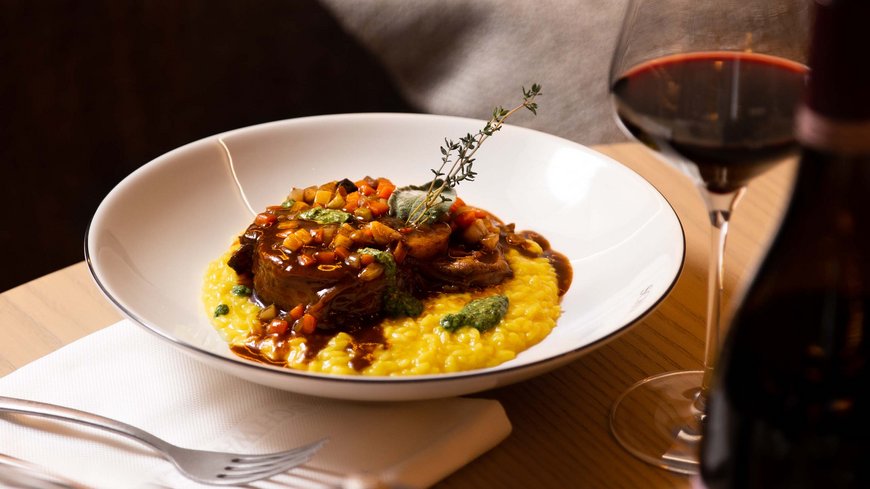 Exzellent essen in diesem Restaurant in Sterzing Risotto mit Fleisch und Gemüse auf weißem Teller, daneben Glas Rotwein und Weinflasche