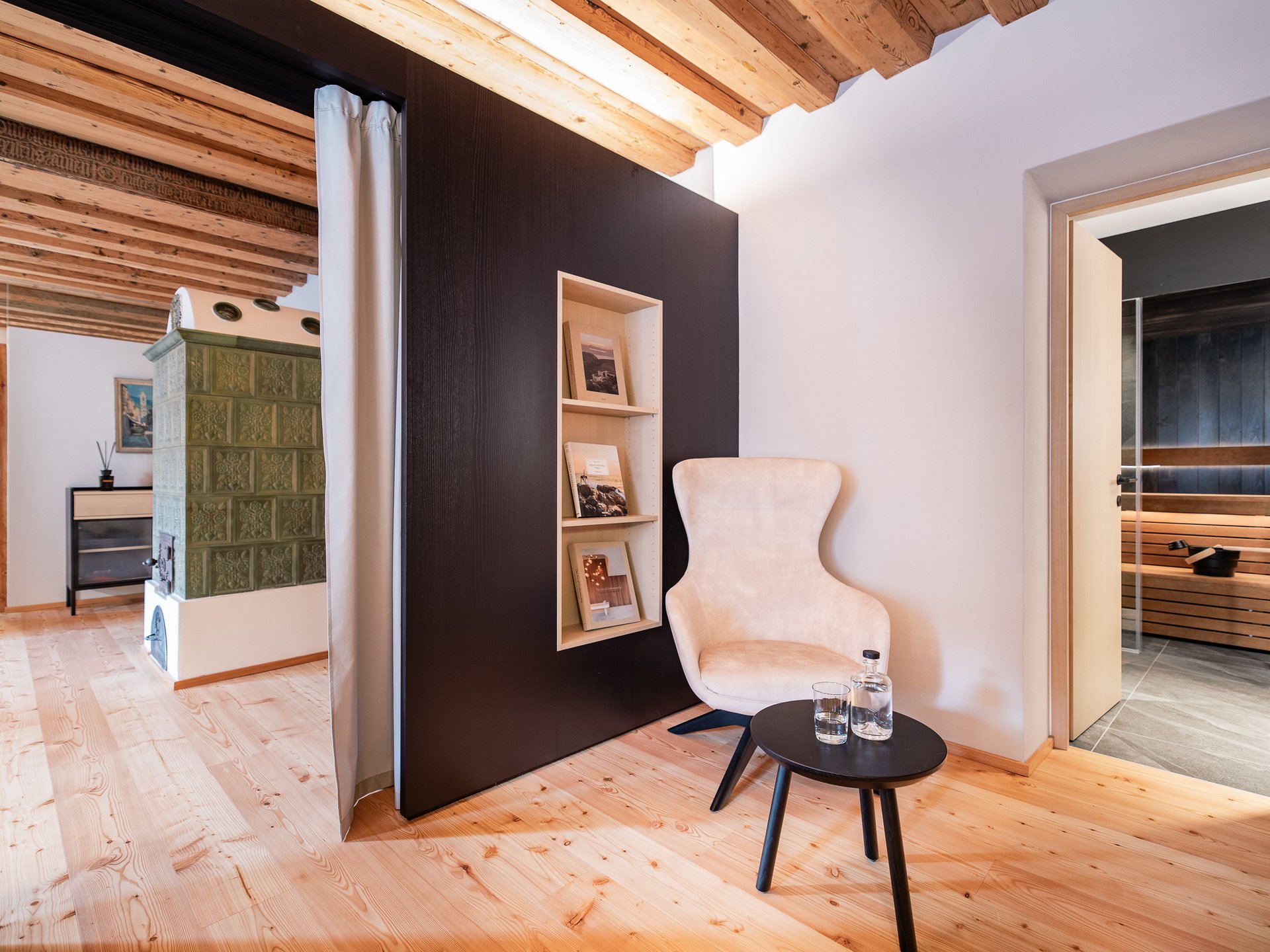 Charmantes Boutique Hotel in Sterzing Gemütlicher Sessel mit Beistelltisch neben offenem Saunaraum in modernem Holzinterieur