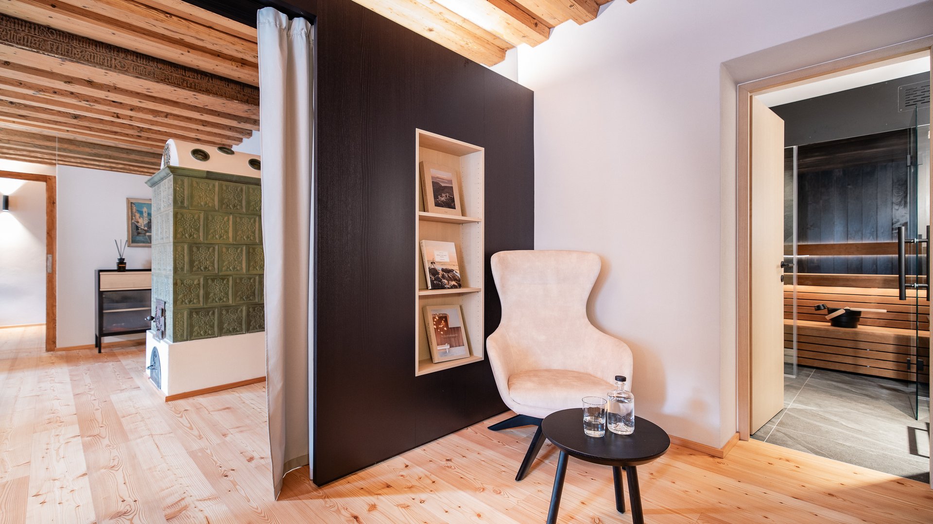 Schwarzer Adler Sterzing: A historic icon. Reinvented. Gemütlicher Sessel mit Beistelltisch neben offenem Saunaraum in modernem Holzinterieur