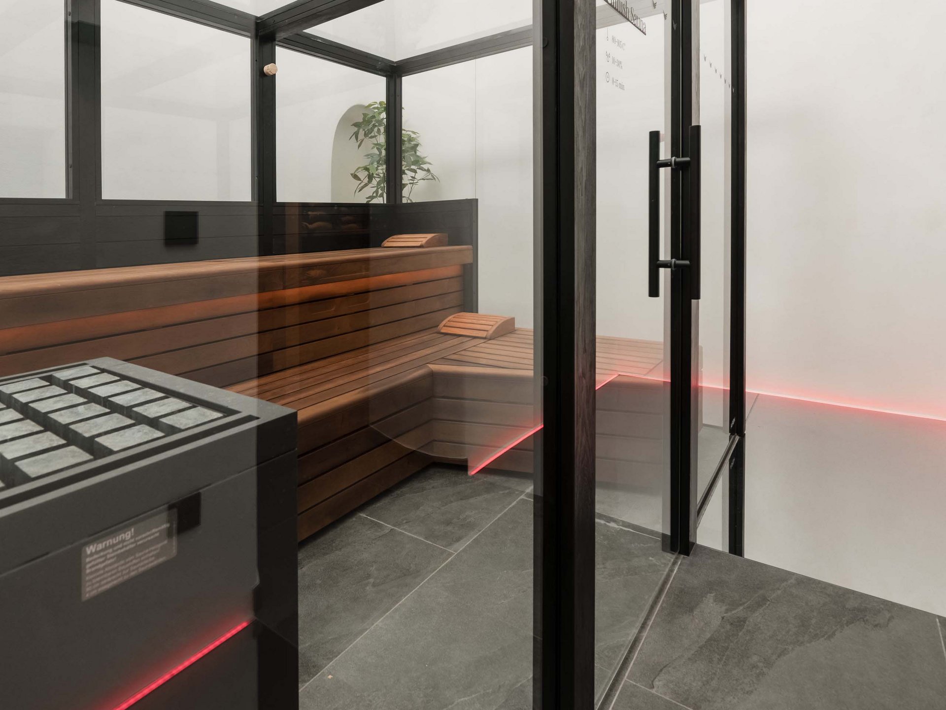 Well-being at the Schwarzer Adler Modern sauna room with glass walls, wooden benches, and red LED lighting