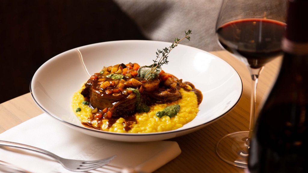 Pamper your palate at this restaurant in Sterzing Risotto with meat and vegetables on a white plate, red wine glass and bottle nearby