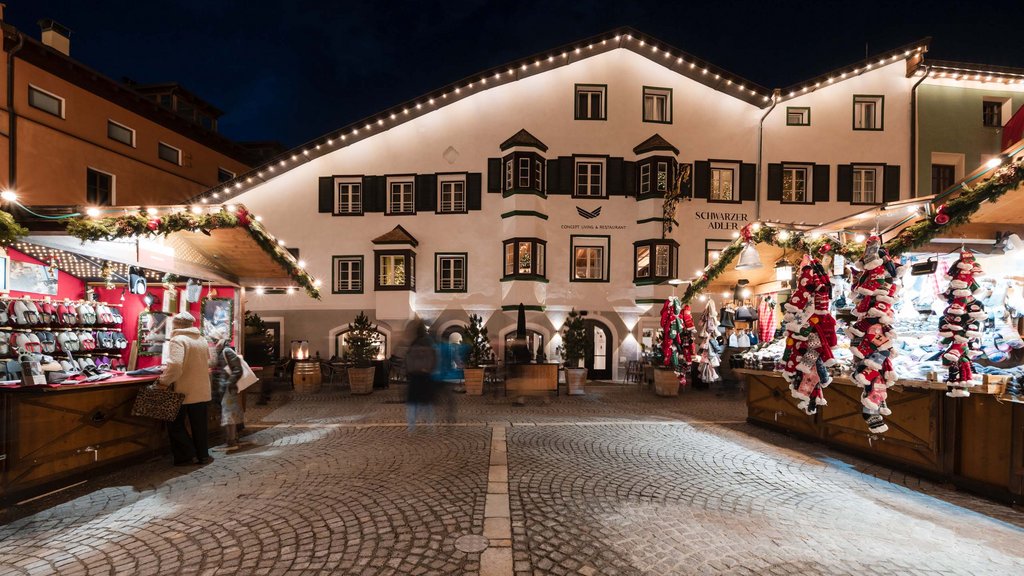 The laid-back town on the Isarco/Eisack river Christmas market stalls with warm lights in front of a lit historic building at night