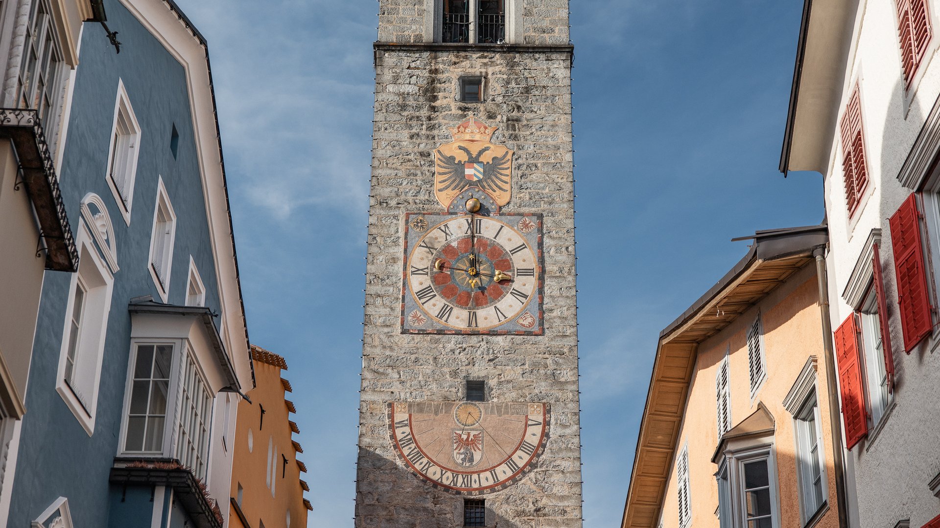 Sights and attractions in and around Sterzing Historic stone clock tower with two large dials amidst colorful buildings
