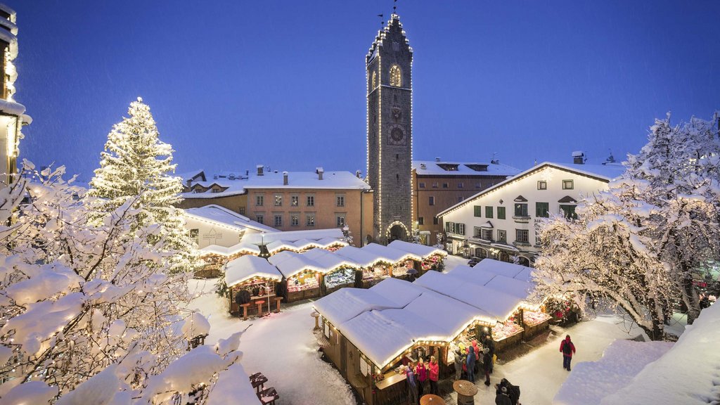 The laid-back town on the Isarco/Eisack river Nighttime Christmas market with snow-covered stalls and illuminated tower