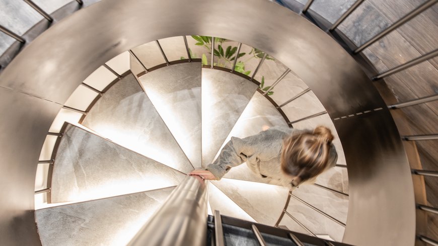 Schwarzer Adler Sterzing: A historic icon. Reinvented. Frau steigt eine beleuchtete Wendeltreppe hinab
