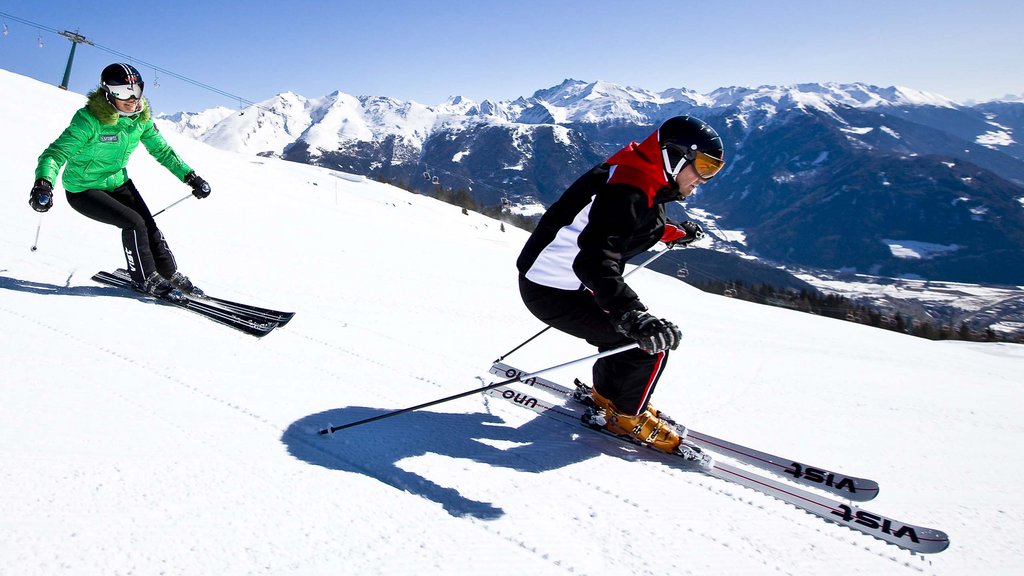 Get your body moving! Two skiers skiing down a snowy slope with mountains in the background