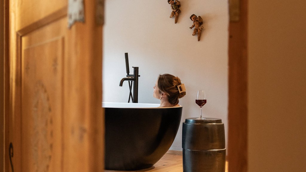 Schwarzer Adler Sterzing: A historic icon. Reinvented. Frau entspannt in schwarzer Badewanne, mit Weinglas auf Hocker, gesehen durch Tür