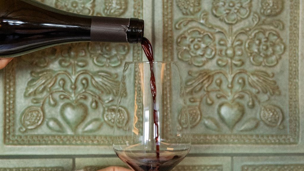 Schwarzer Adler Sterzing: A historic icon. Reinvented. Roter Wein wird aus einer Flasche in ein Weinglas gegossen vor grüner Wand