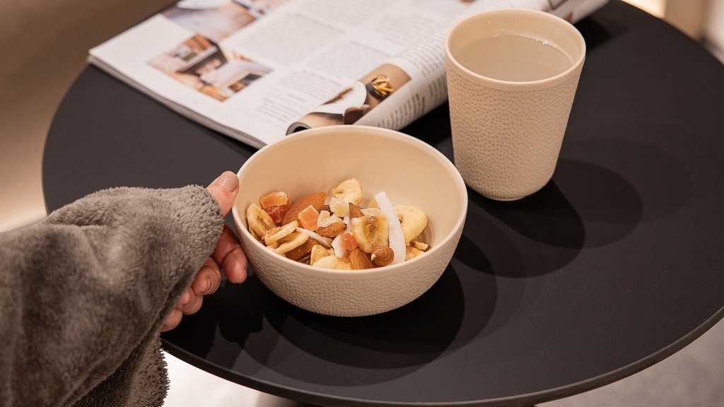 Well-being at the Schwarzer Adler Hand holding bowl of nuts, water cup and magazine on black table