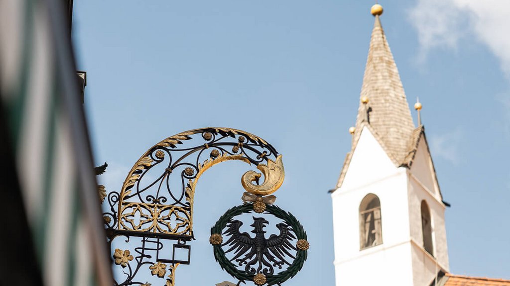 The perfect location for your apartment in Sterzing Sign with black eagle and church tower under blue sky