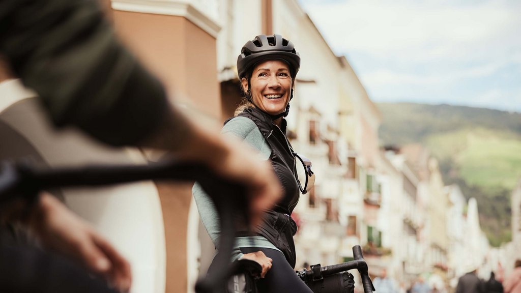 Cooles Rennradhotel in Südtirol Frau mit Fahrradhelm lächelt beim Radfahren in der Stadt