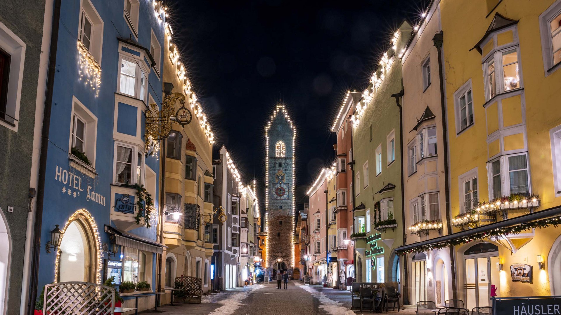 The laid-back town on the Isarco/Eisack river Lit pedestrian street with colorful historic buildings and clock tower at night