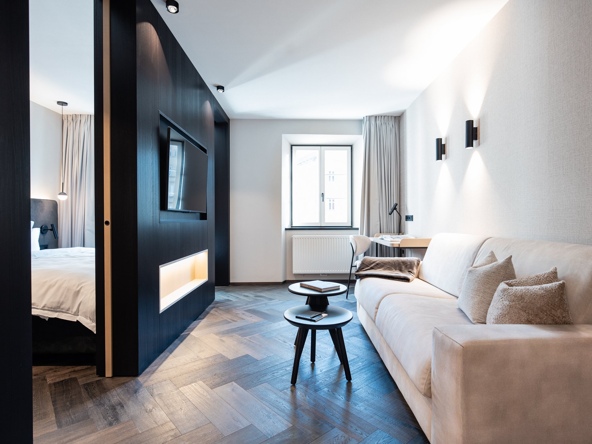 Charmantes Boutique Hotel in Sterzing Modern eingerichtetes Wohnzimmer mit Sofa, Couchtischen und Schlafzimmer im Hintergrund