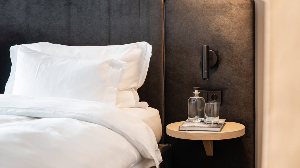 Schwarzer Adler Sterzing: A historic icon. Reinvented. Nahaufnahme eines Bettes mit weißen Kissen und kleinem Beistelltisch mit Wasserflasche