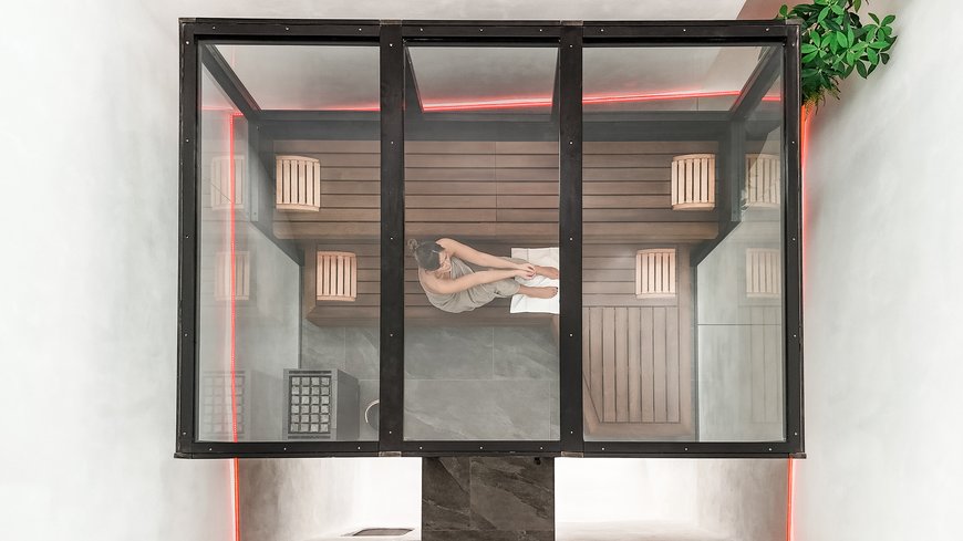 Schwarzer Adler Sterzing: A historic icon. Reinvented. Frau in Handtuch sitzt in moderner Sauna mit Glasdach und roter LED-Beleuchtung