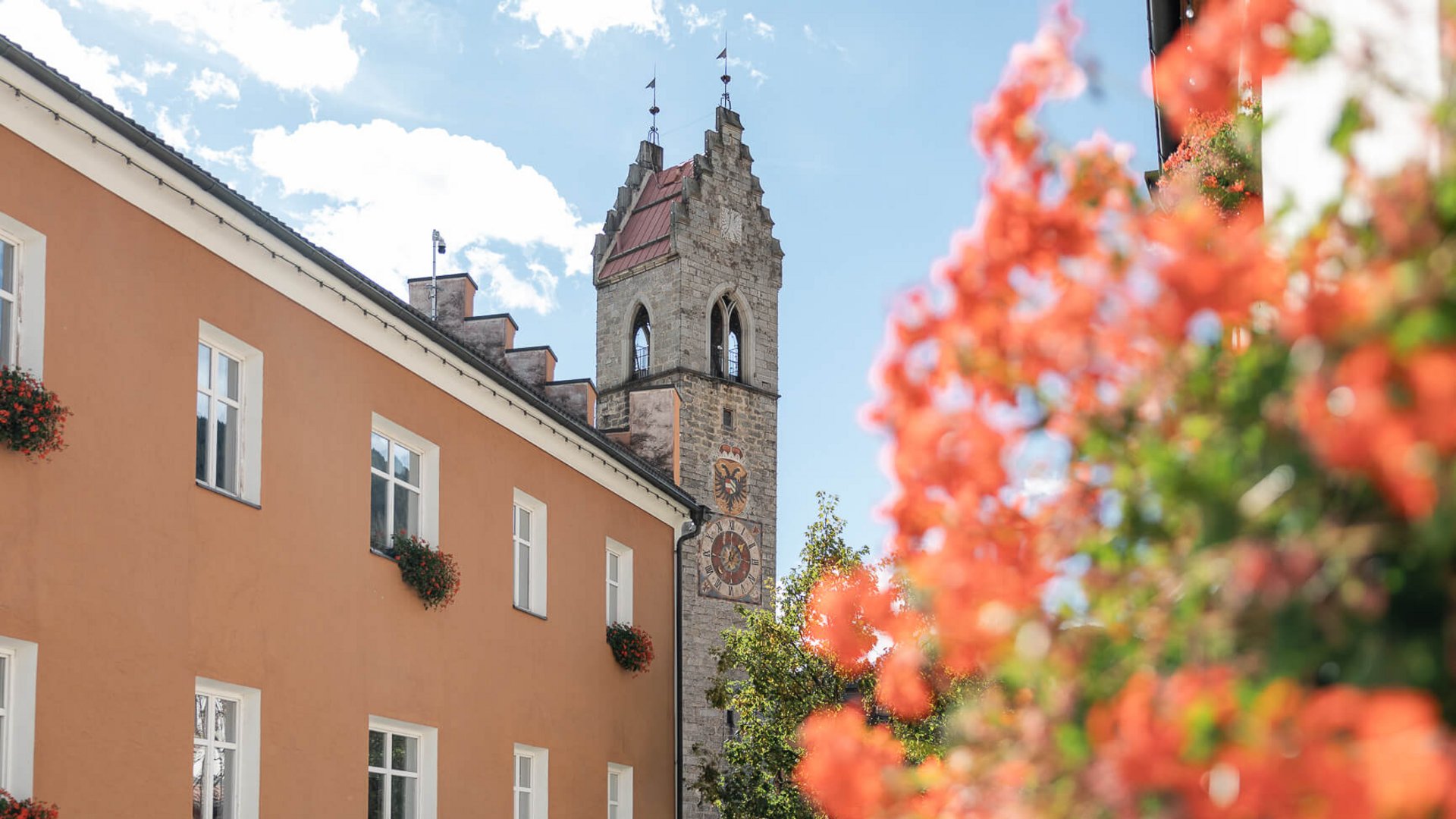 The perfect location for your apartment in Sterzing Clock tower on historic building next to orange house with flowers on windows