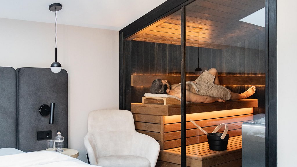 Schwarzer Adler Sterzing: A historic icon. Reinvented. Person entspannt in Sauna neben modernem Schlafzimmer mit weißem Bett