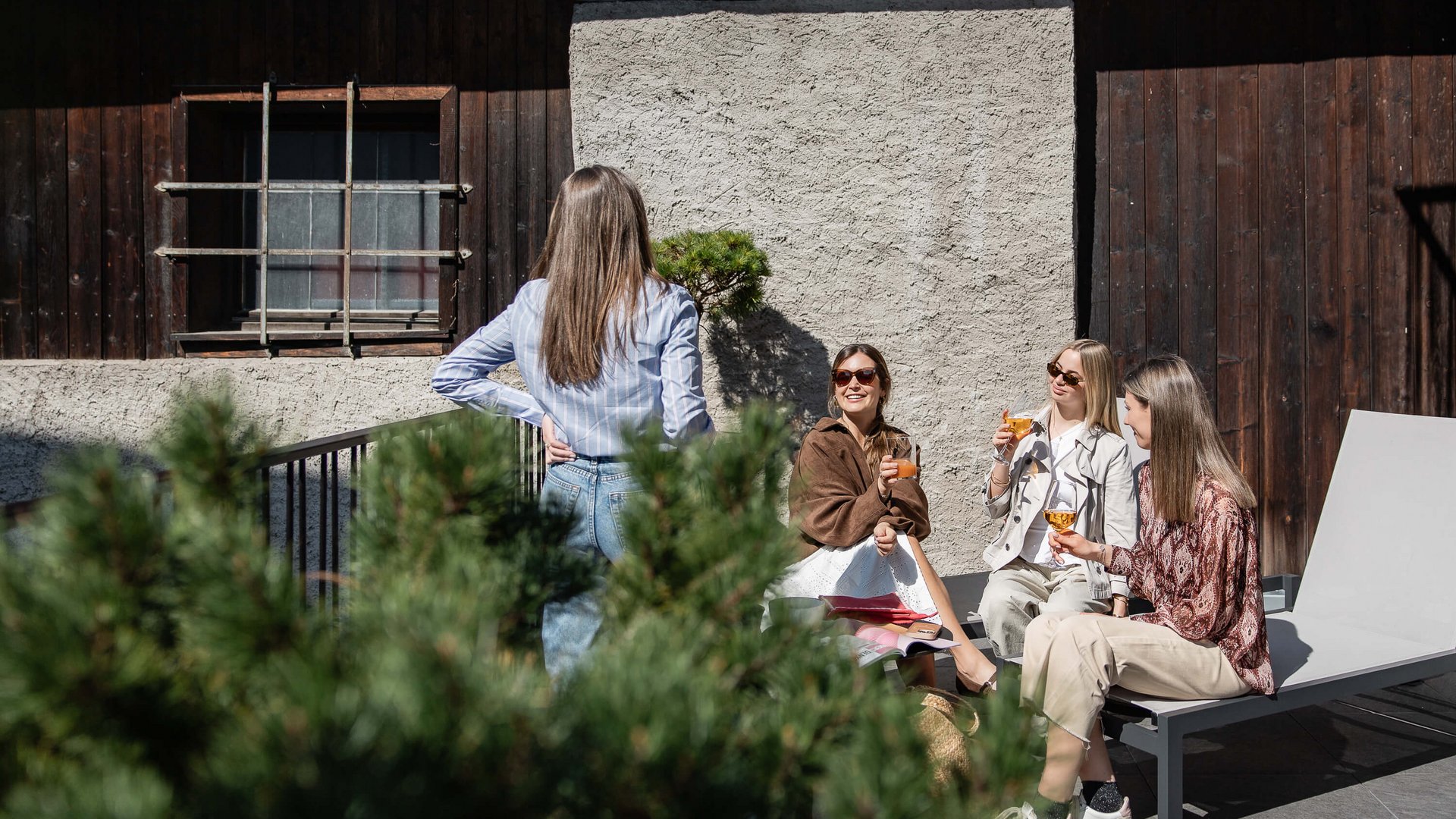 Schwarzer Adler Sterzing: A historic icon. Reinvented. Vier Frauen trinken gemeinsam Getränke auf einer Terrasse im Sonnenschein