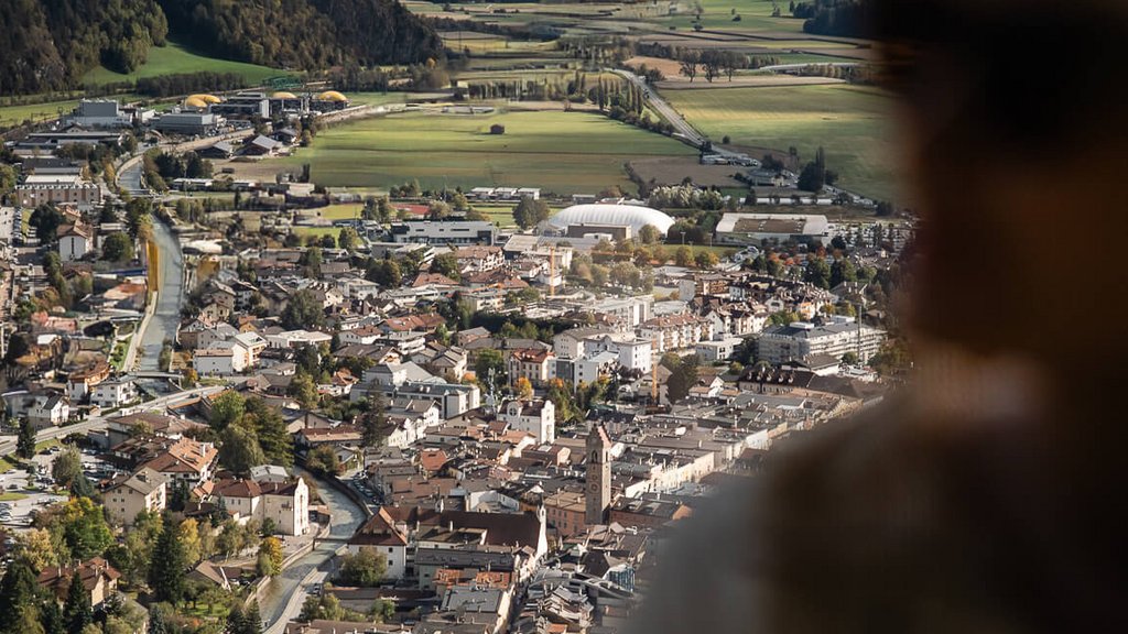 The perfect location for your apartment in Sterzing View of an alpine town with mountains and fields, blurred person in foreground
