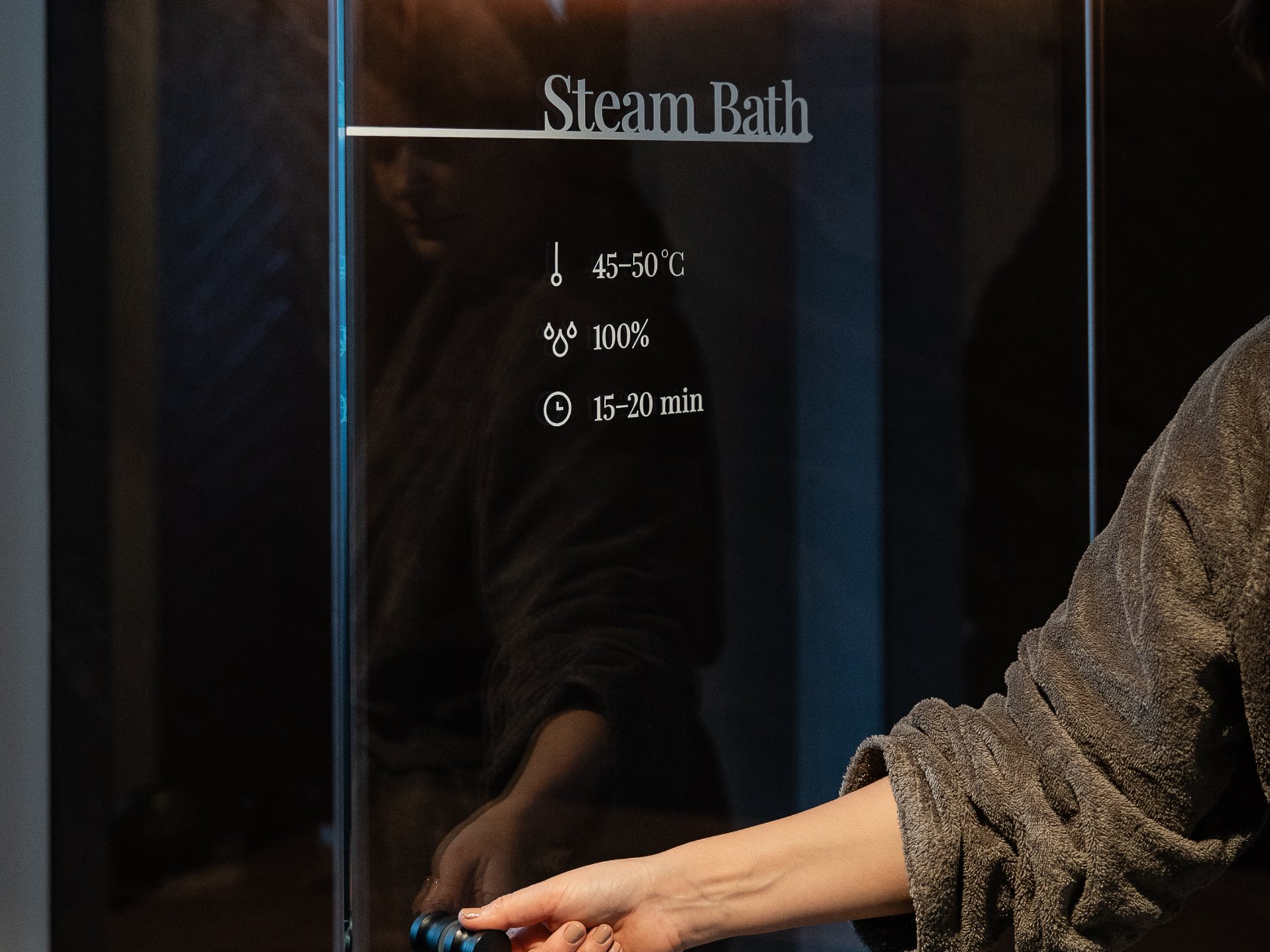 Well-being at the Schwarzer Adler Hand opening glass door of illuminated steam bath in spa