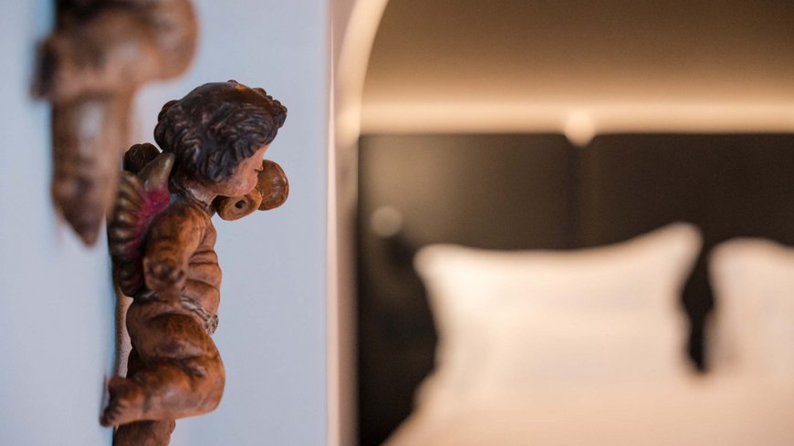 Schwarzer Adler Sterzing: A historic icon. Reinvented. Holzengel an einer Wand neben einem unscharfen Bett im Hintergrund