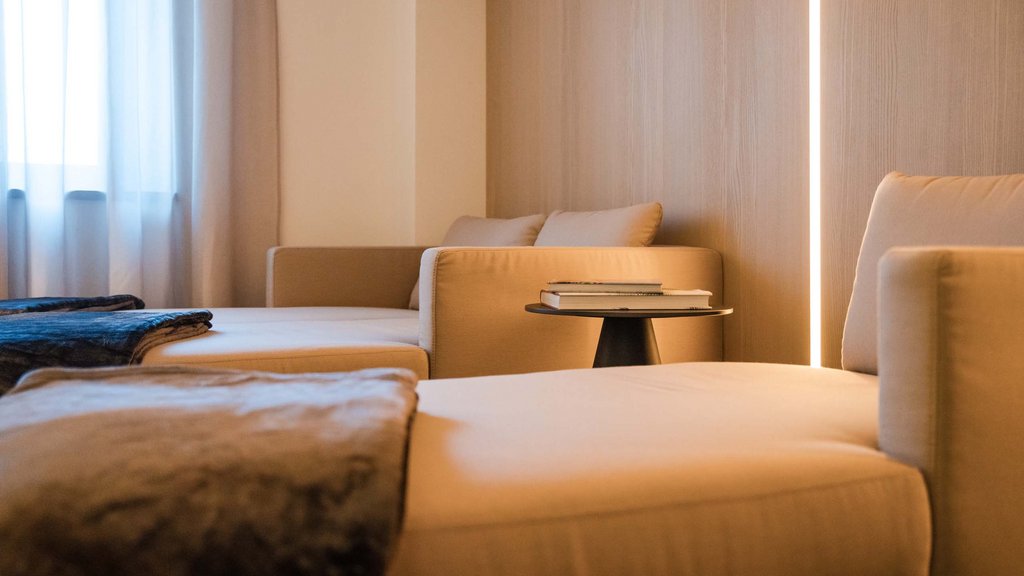 Well-being at the Schwarzer Adler Bright living room with comfortable beige sofas, blanket, and small side table with books