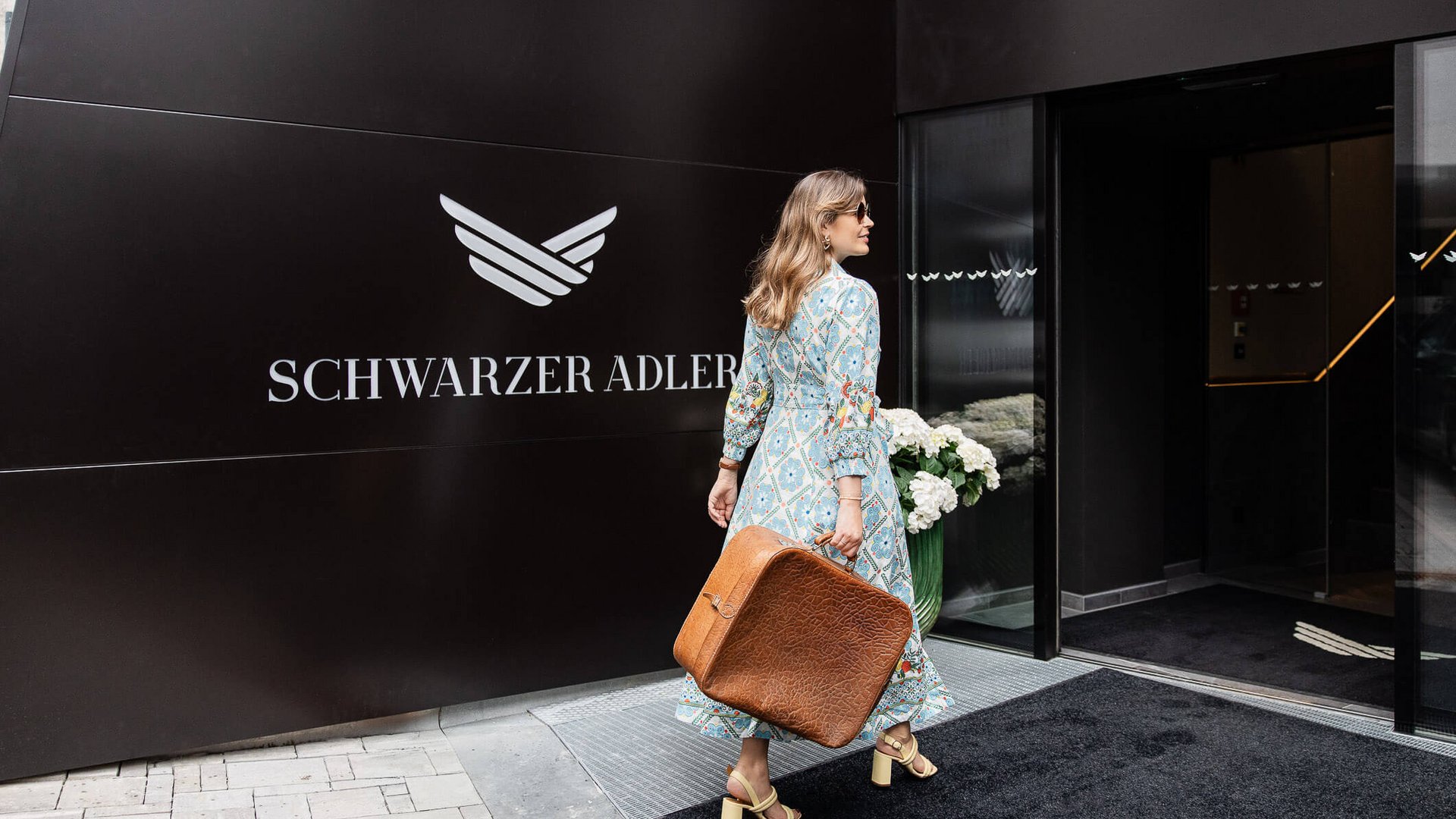 Schwarzer Adler Sterzing: A historic icon. Reinvented. Frau mit braunem Koffer geht ins Hotel Schwarzer Adler