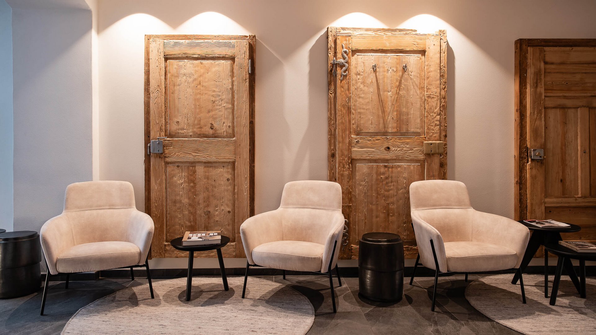 Schwarzer Adler Sterzing: A historic icon. Reinvented. Drei beige Sessel vor drei hellen Holztüren an einer Wand mit runden Teppichen