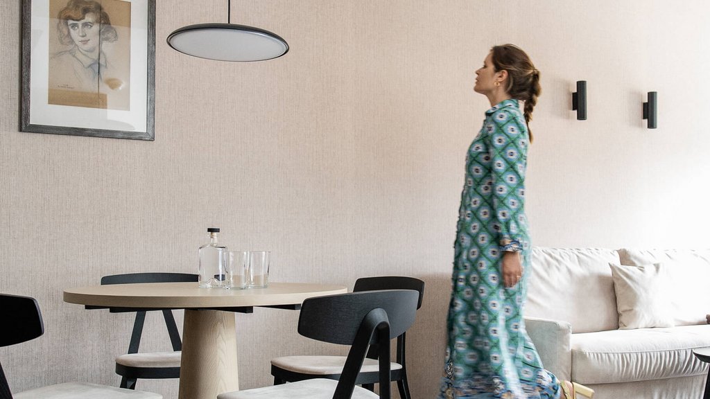 Schwarzer Adler Sterzing: A historic icon. Reinvented. Frau in blauem Kleid geht in modernem Esszimmer mit Holzstuhl und Tisch