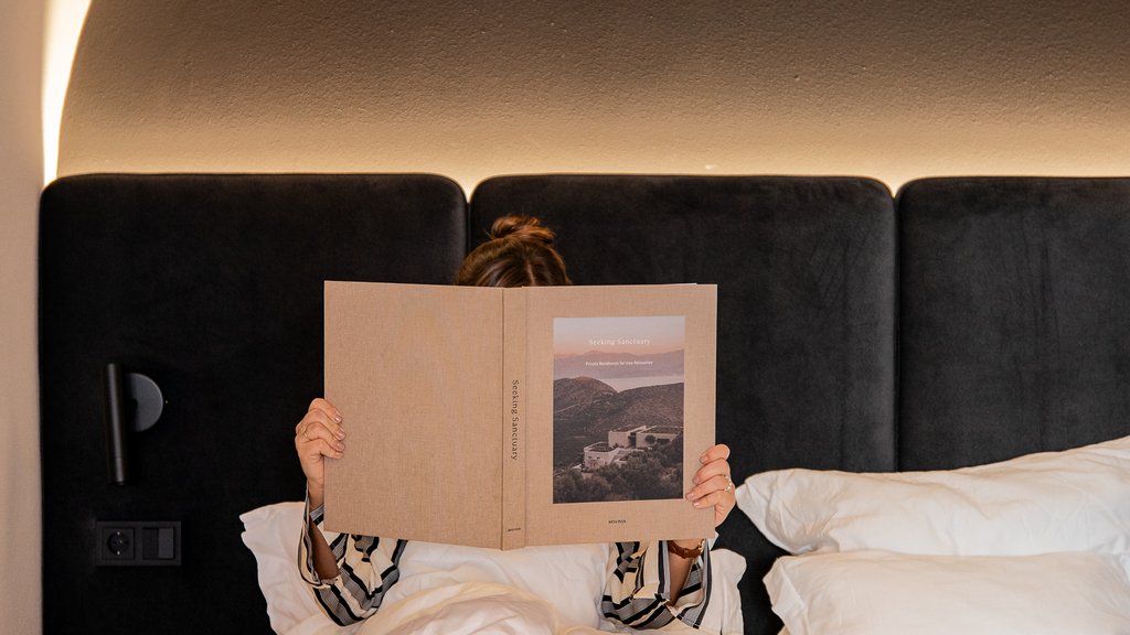 Schwarzer Adler Sterzing: A historic icon. Reinvented. Person liest Buch im Bett mit schwarzem Kopfteil und warmem Lichtbogen