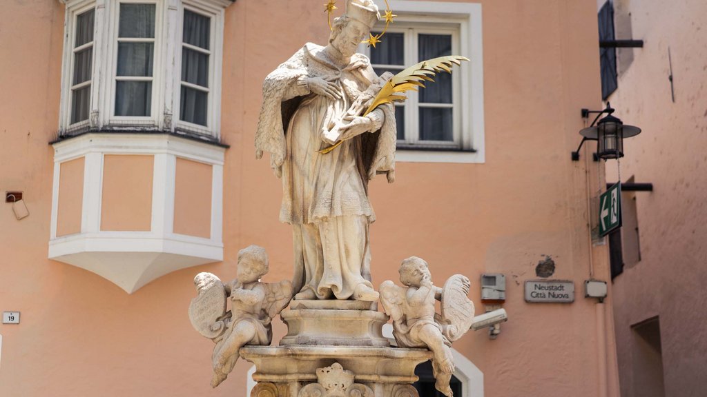 The laid-back town on the Isarco/Eisack river Saint statue with halo and golden feather in old town in front of pink building