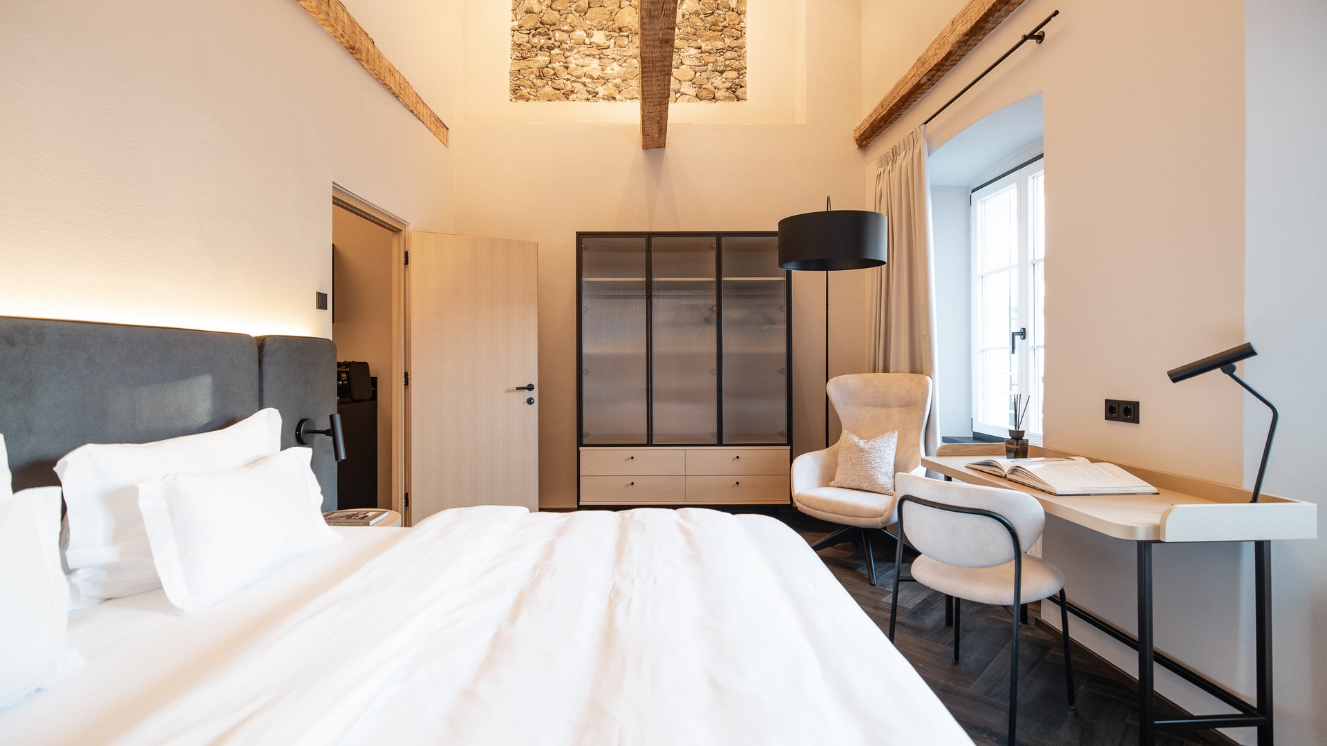 Charmantes Boutique Hotel in Sterzing Modernes Schlafzimmer mit hellem Bett, grauem Kopfteil und Schreibtisch am Fenster
