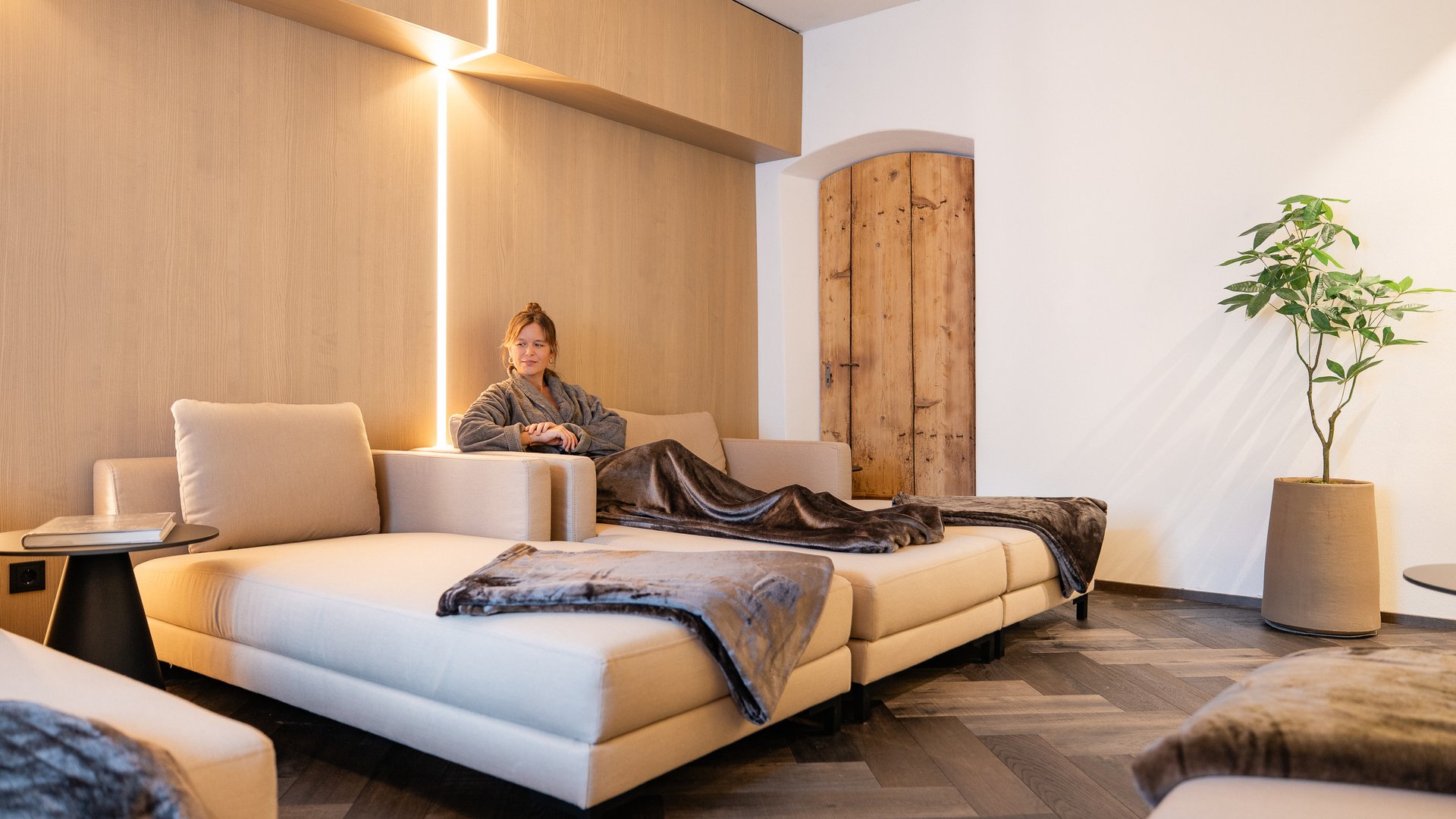Schwarzer Adler Sterzing: A historic icon. Reinvented. Frau entspannt auf beige Sofa in gemütlichem, modernem Wohnzimmer